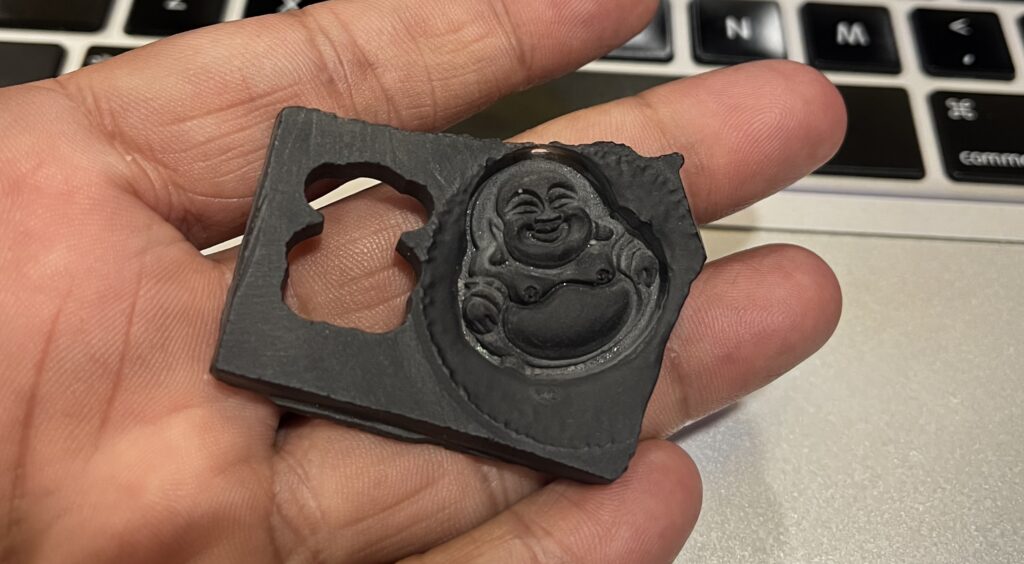 CNC gemstone carving of a laughing buddha on a black onyx slab.